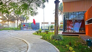 Uma trilha pavimentada conduz a um edifício de design moderno, cercado por vegetação e palmeiras.