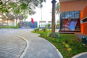 Un camino pavimentado que lleva a un edificio de diseño moderno, rodeado de follaje y palmeras.