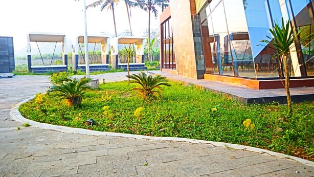 Um edifício moderno com amplas janelas de vidro, um caminho pavimentado e pequenas palmeiras.