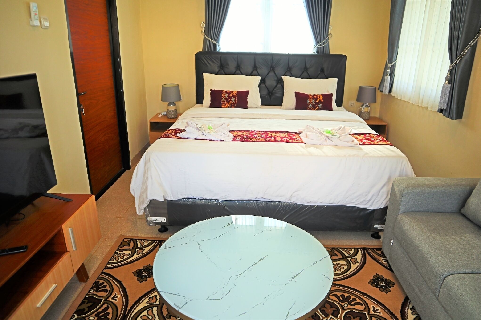 A hotel room with a bed, bedside tables, a TV, a sofa, and a round table.