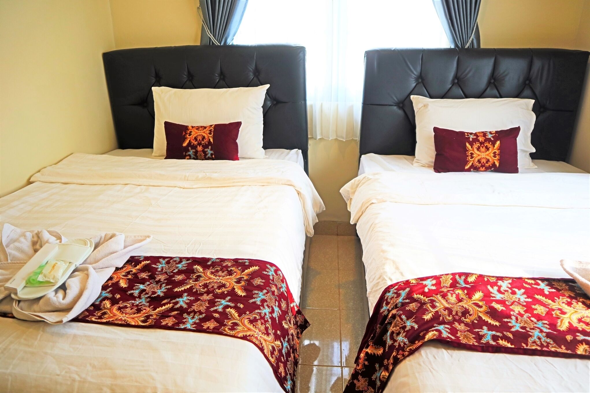 Two twin beds with black headboards, white bedding, and red patterned bedspreads.
