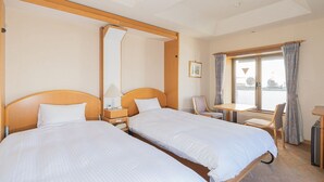 Hotelkamer met twee enkele bedden, een kleine tafel, een stoel, een bureau en een raam met gordijnen.