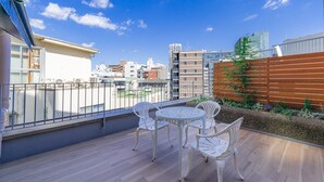 Een balkon met een houten vloer, witte rieten stoelen en een klein rond tafeltje.