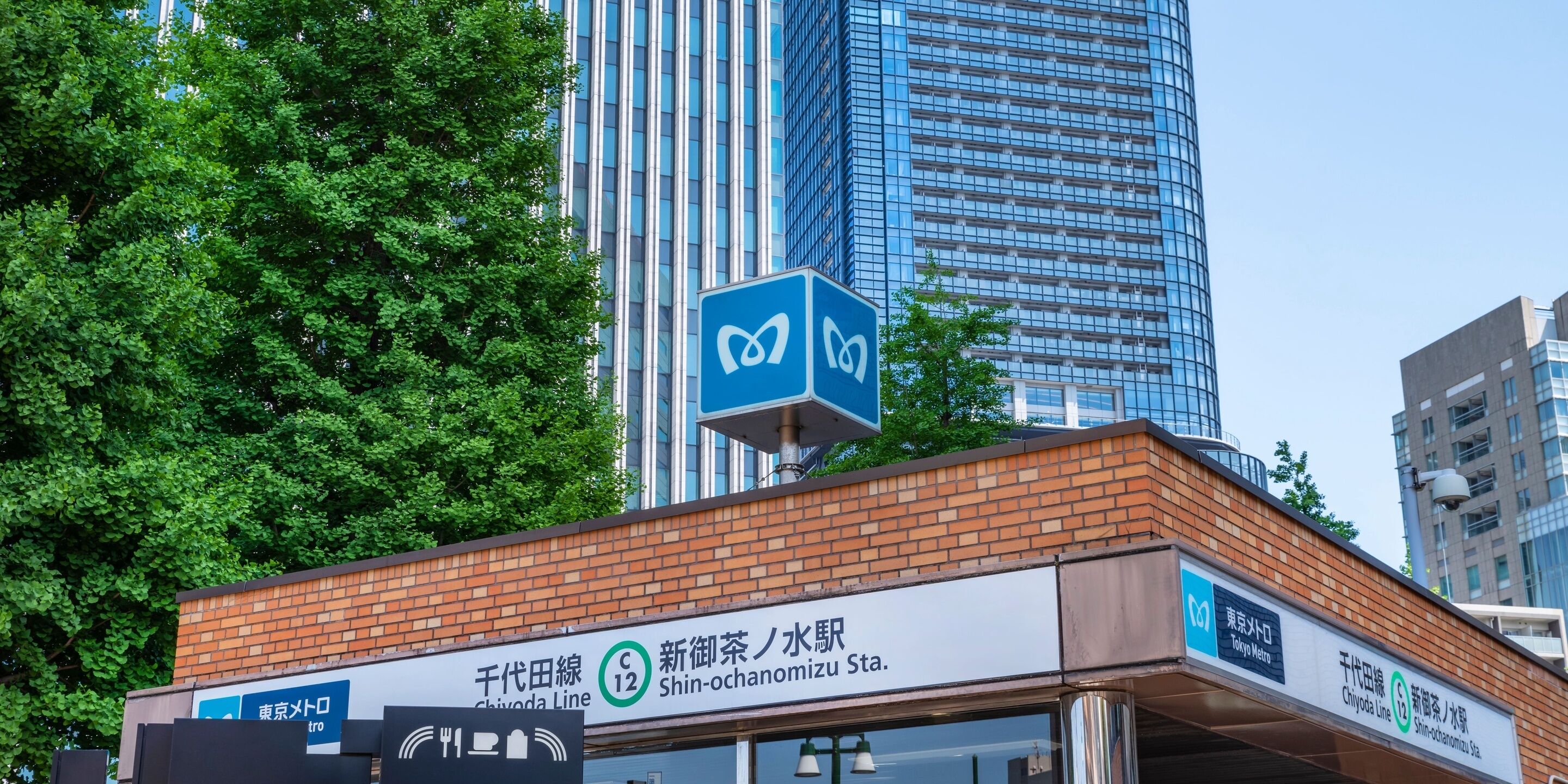 A building with a sign for the Chiyoda Line and a nearby tree.
