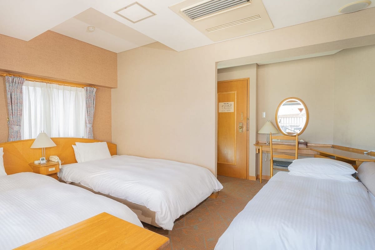 Een hotelkamer met twee enkele bedden, een houten nachtkastje met een lamp, een kleine tafel en een spiegel.