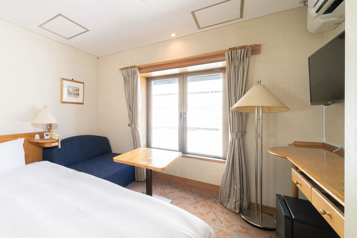 Een hotelkamer met een bed, een bureau, een stoel, een televisie en een raam met gordijnen.