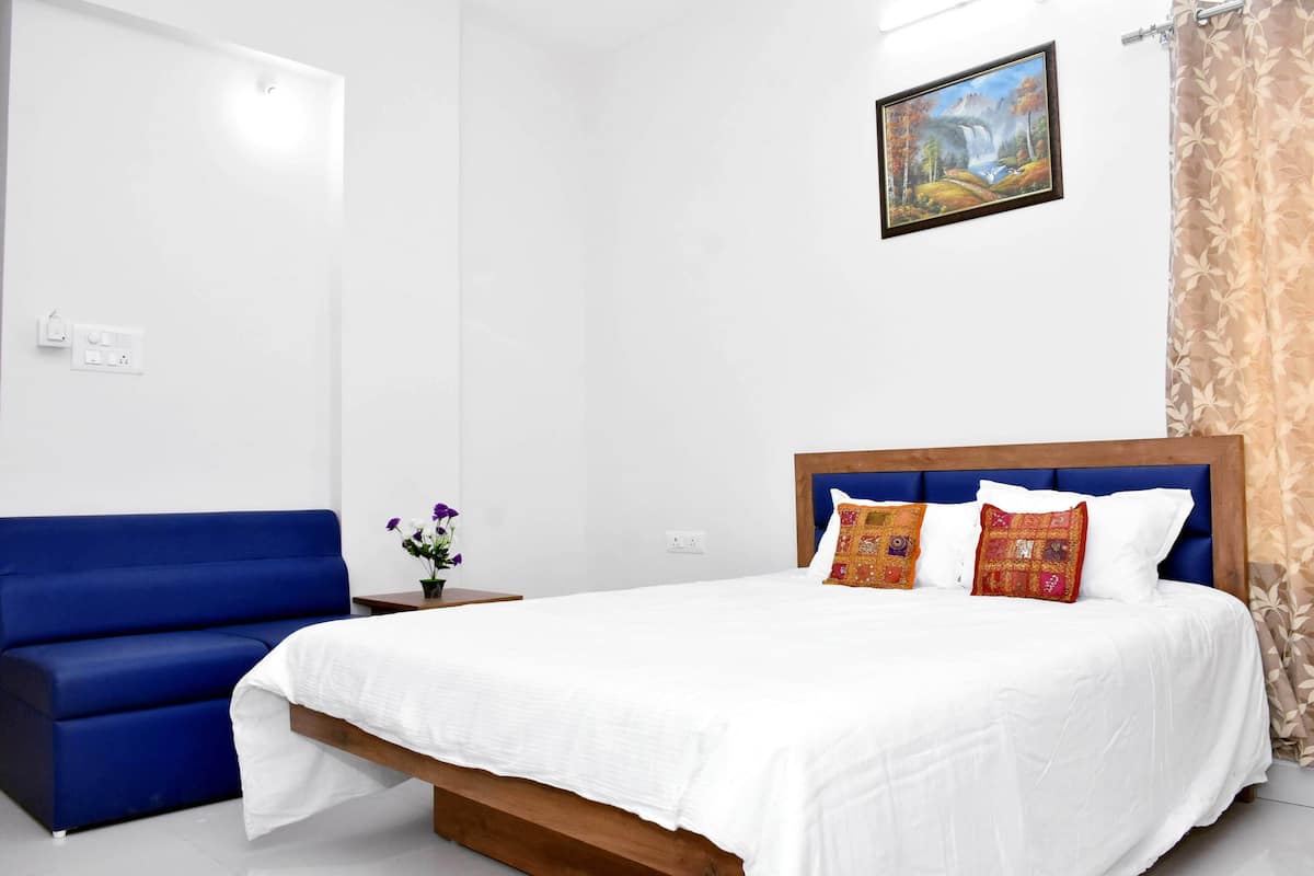 Un dormitorio con una cama, un sofá azul, una mesita con un jarrón de flores y un cuadro en la pared.