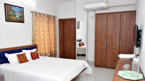 A hotel room with a bed, curtains, a wardrobe, a TV, and a small table with bottles. - Hotel Pride Arena (Bhopal)