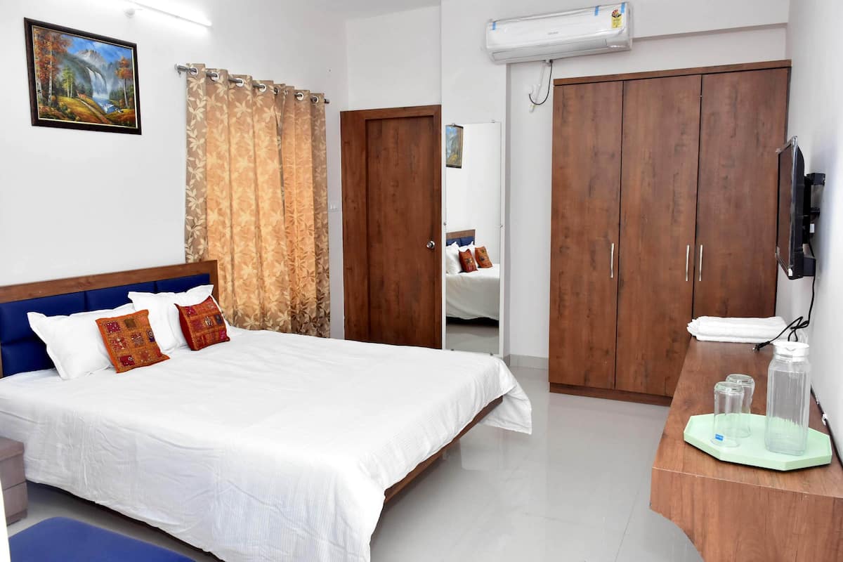 Habitación de hotel con cama, cortinas, armario, televisor y una mesita con botellas.