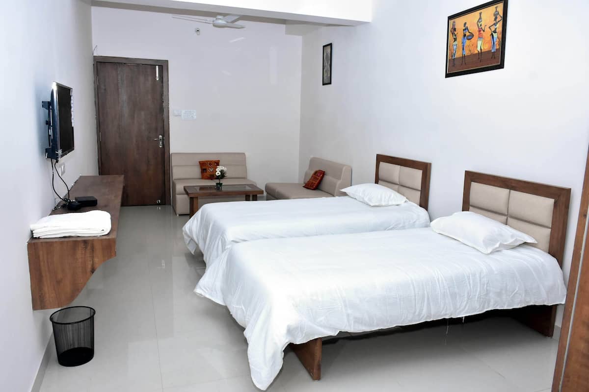 Habitación de hotel con dos camas, un sofá, una mesita, un televisor y un cubo de basura.