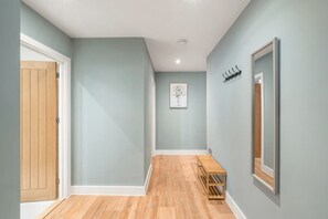 A hallway with light blue walls, a wooden door, a bench, and a coat rack.