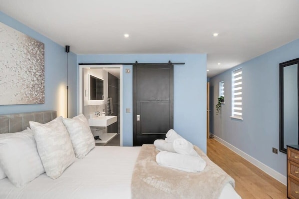 A modern bedroom with a bed, pillows, a fluffy blanket, and a bathroom visible through an open door. - Modern Apartment with Parking nr Seafront (Paignton)