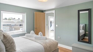 Una camera da letto con un letto, una finestra, una porta, uno specchio e vista sui palazzi.