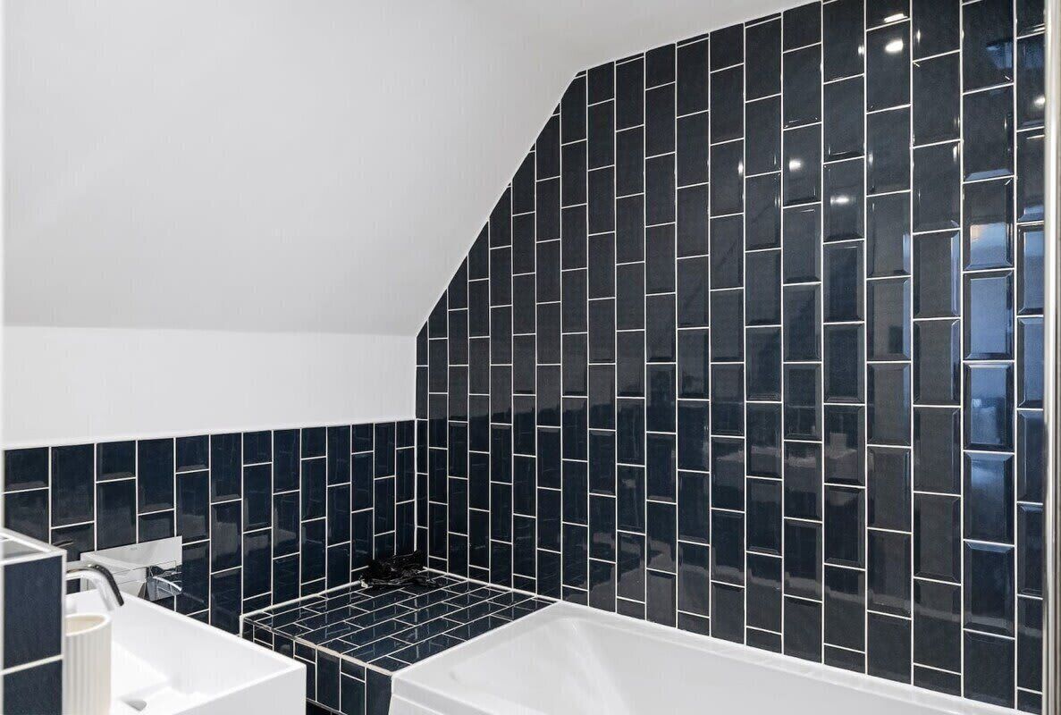Une salle de bain moderne avec des murs recouverts de carreaux bleu foncé, une baignoire blanche et un lavabo blanc.