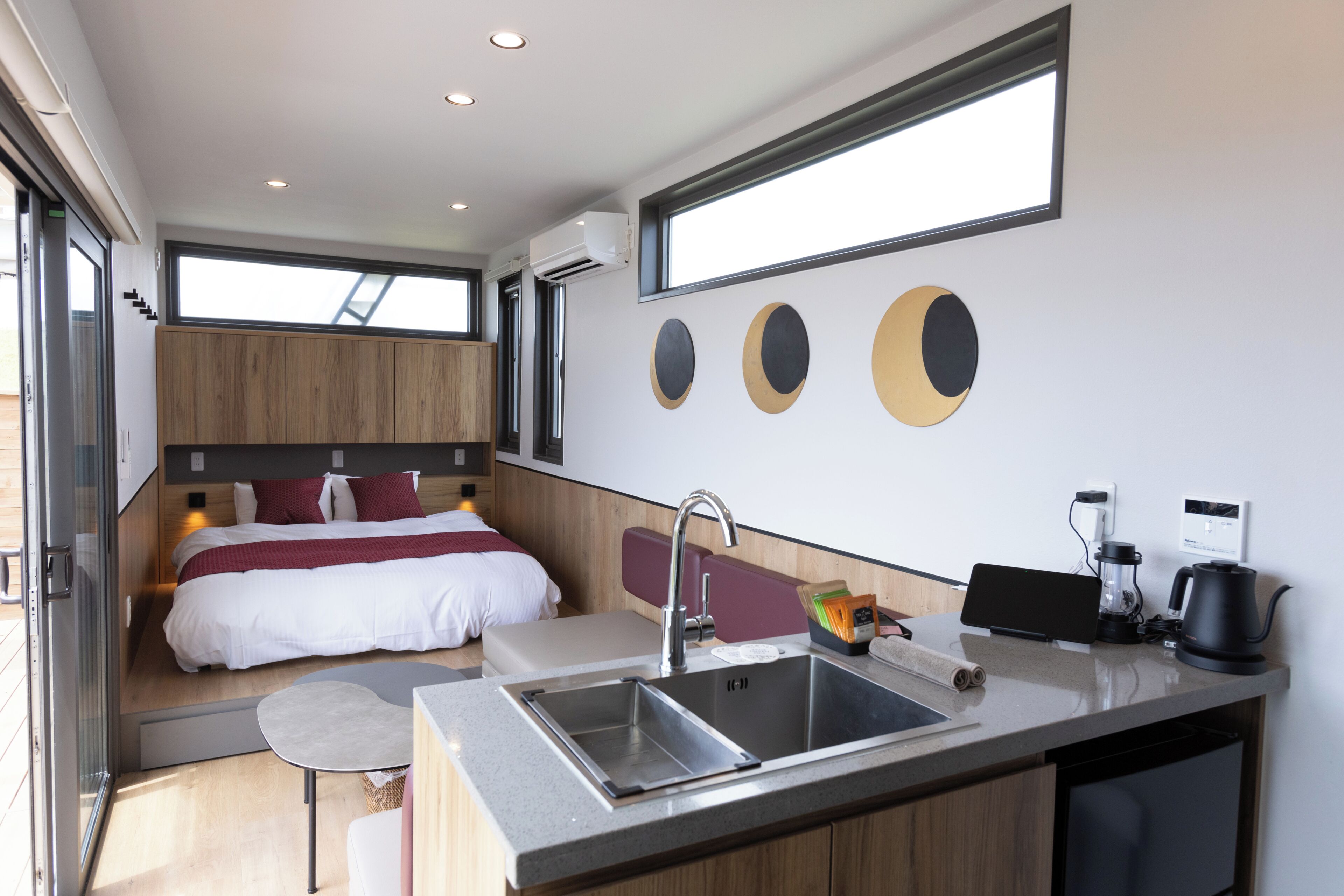 Una habitación de hotel moderna con cama, un pequeño rincón de descanso, una kitchenette con lavaplatos y un amplio ventanal.