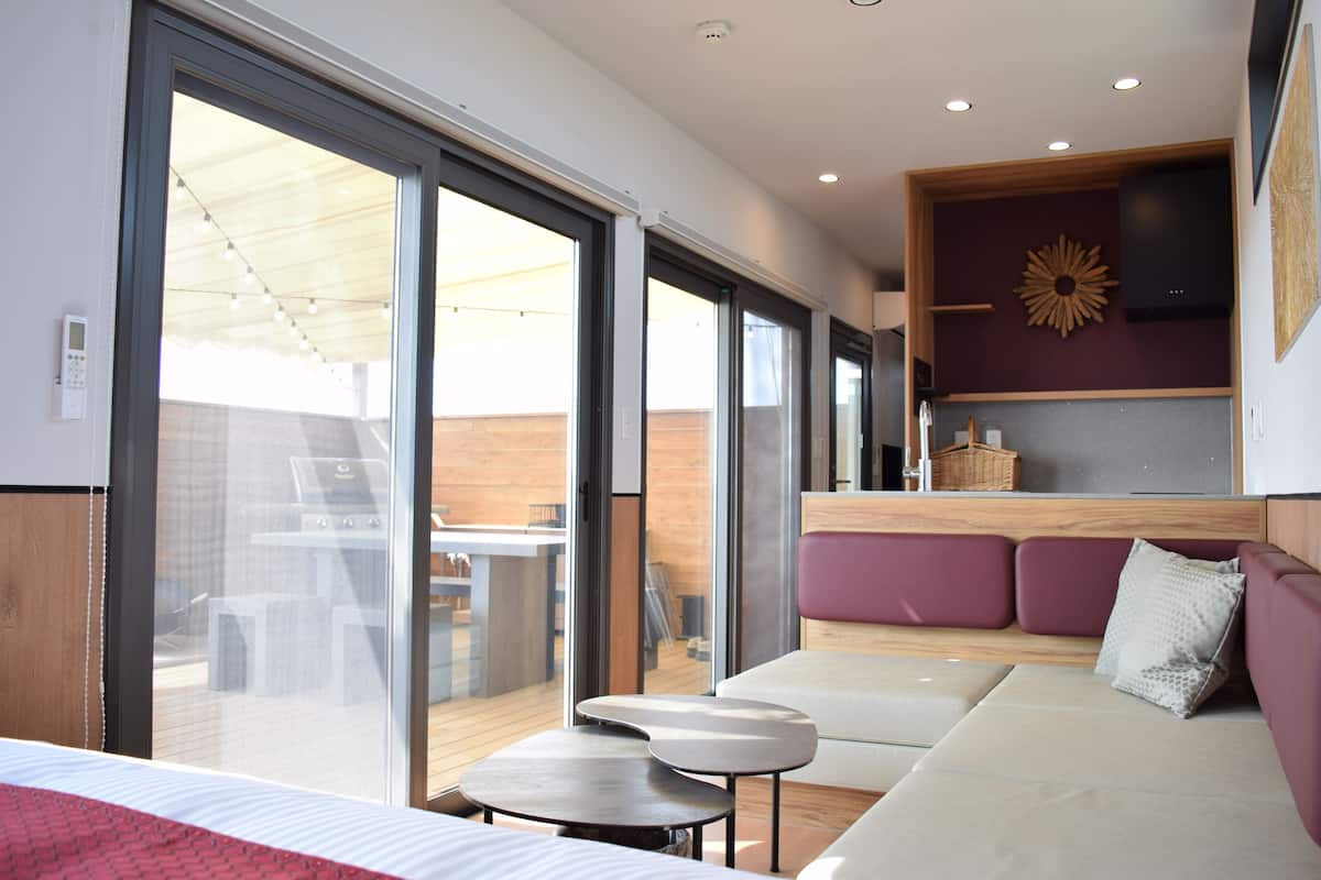 A modern interior with a sofa, a small table, and a bench. There is a sliding glass door leading to an outdoor area.