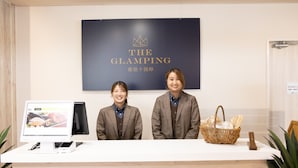 Un mostrador de recepción con una pantalla digital, un cartel que dice "THE GLAMPING" y una cesta de mimbre con servilletas.