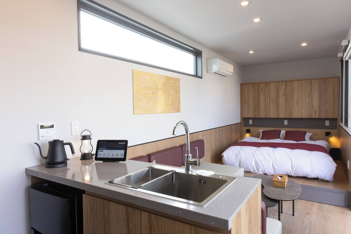 A compact hotel room with a kitchenette, a bed, and a small seating area.