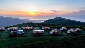 Una hilera de cabañas tipo motorhome con terrazas adjuntas, frente a un paisaje montañoso al atardecer.