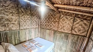 Ein Zimmer mit Bett, einer Pendelleuchte und Bambuswänden.