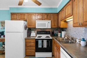 A kitchen with wooden cabinets, a white refrigerator, a microwave, a stove, and a sink.