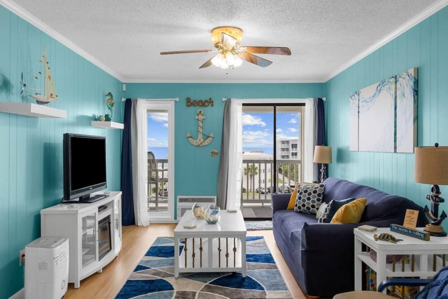 A room with a television, a white cabinet, a blue sofa, and a ceiling fan.
