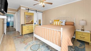 A bedroom with a bed, nightstands, a dresser, a ceiling fan, and a television. - Blue's Oceanview 2Bdrm- Pool, Peaceful Balcony (Myrtle Beach)