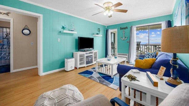 A living room with a television, white cabinet, blue sofa, and a ceiling fan. - Blue's Oceanview 2Bdrm- Pool, Peaceful Balcony (Myrtle Beach)