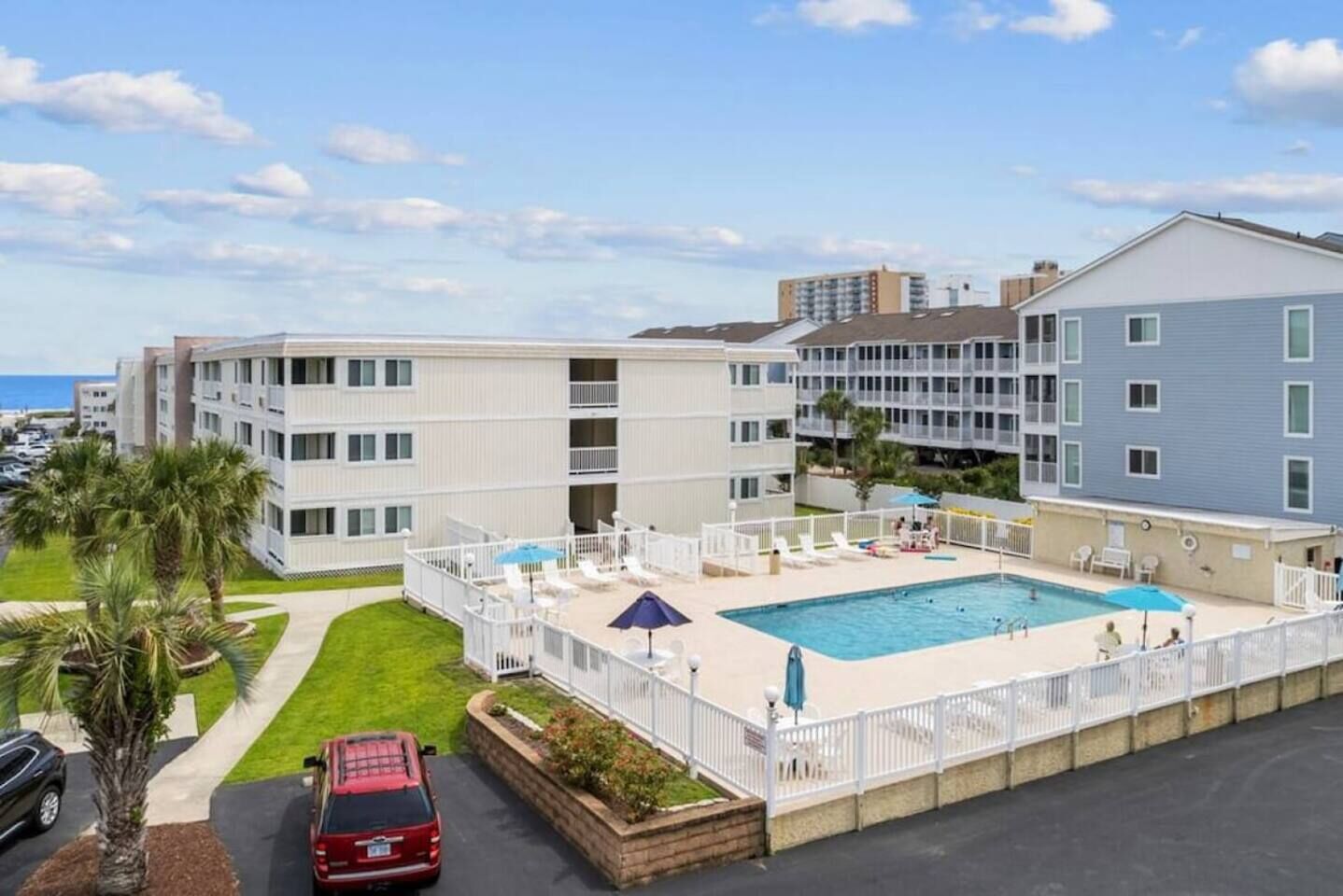A multi-story hotel with a swimming pool, outdoor seating, and a parking area.