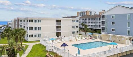 A multi-story hotel with a swimming pool, outdoor seating, and a parking area.