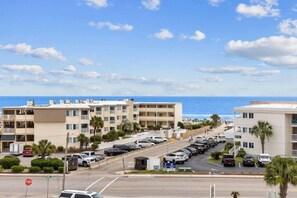 A coastal hotel with multiple floors, a parking lot, and a view of the sea.