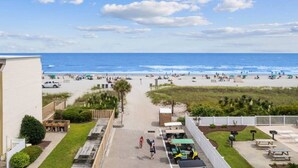 A beach view from a balcony with a clear sky, a sandy beach, and a few people. - Blue's Oceanview 2Bdrm- Pool, Peaceful Balcony (Myrtle Beach)