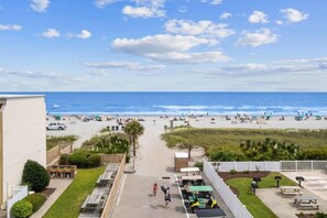 A beach view from a balcony with a clear sky, a sandy beach, and a few people.