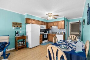 A compact kitchen with wooden cabinets, a white refrigerator, and a dining area with a table set for two.