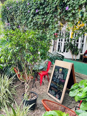 A café with a chalkboard sign, outdoor seating, and potted plants. - Otoya1907 Hotel (San José)