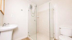 A bathroom with a glass-enclosed shower, a white sink, and a toilet. - Otoya1907 Hotel (San José)
