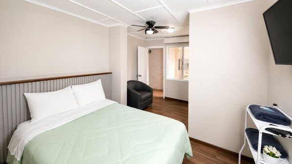 A hotel room with a bed, a chair, a TV, and a ceiling fan.