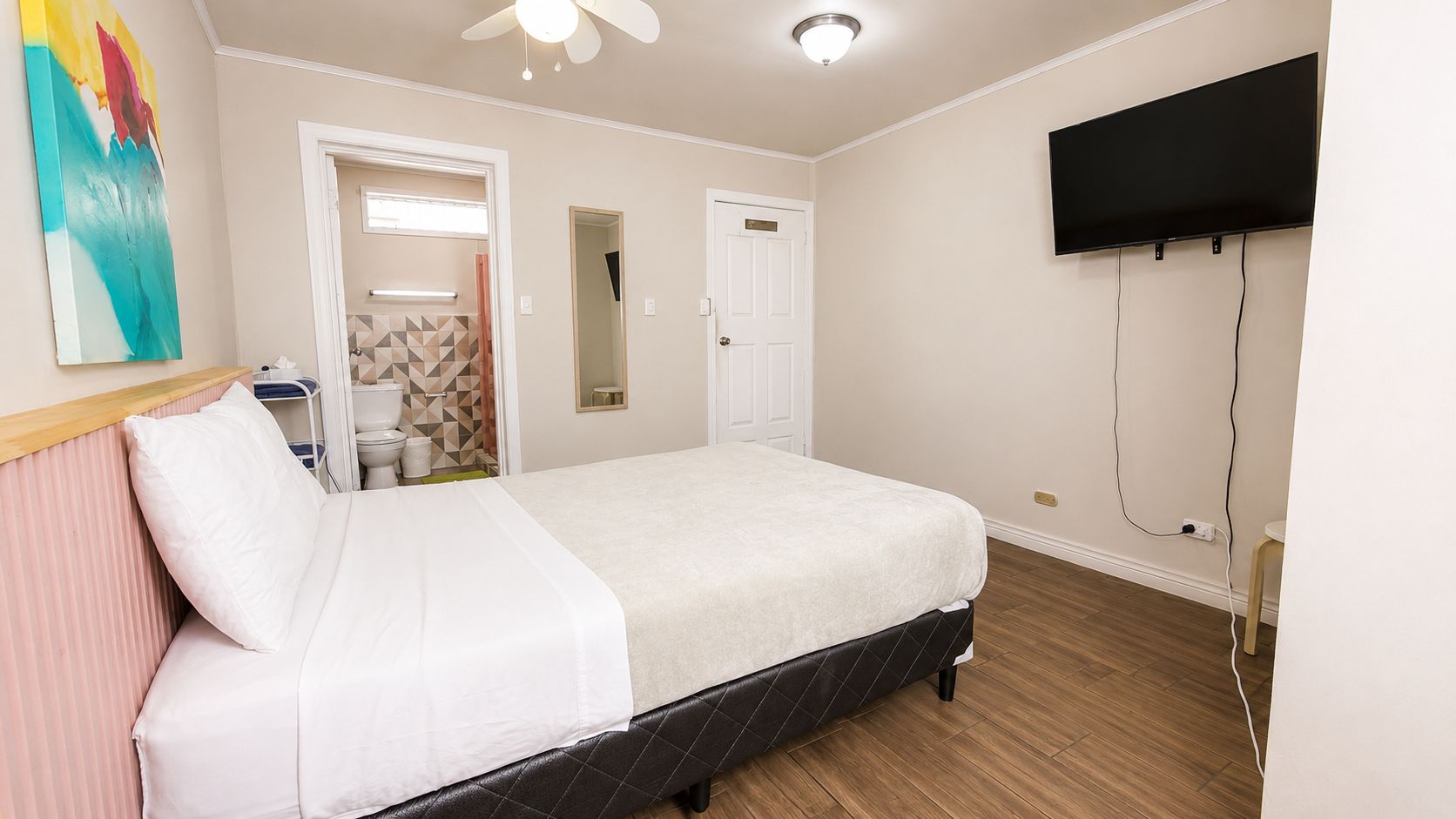 A hotel room with a bed, a television mounted on the wall, and a bathroom visible through an open door.