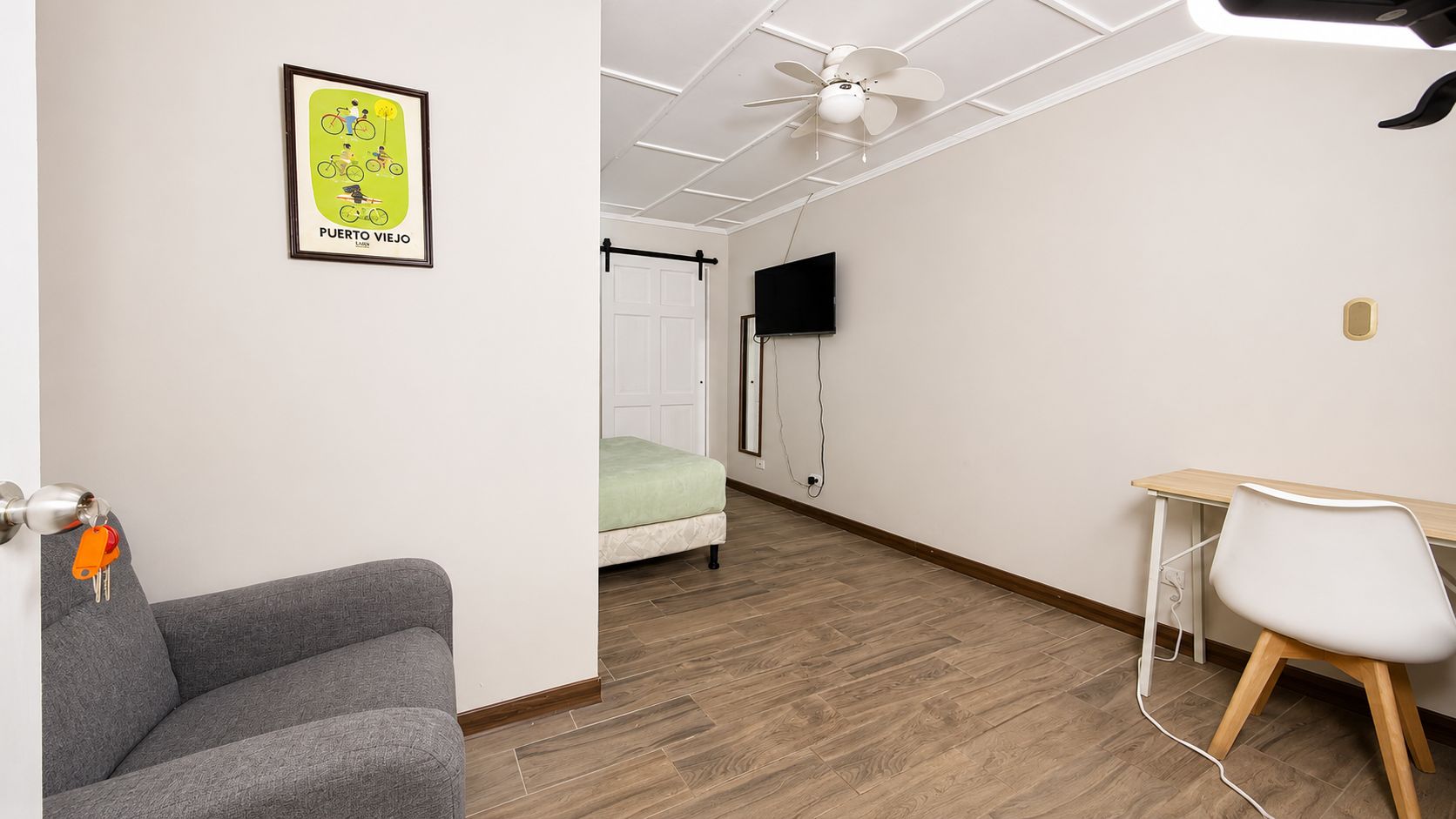 Una habitación con cama, escritorio, silla, televisor y ventilador de techo.