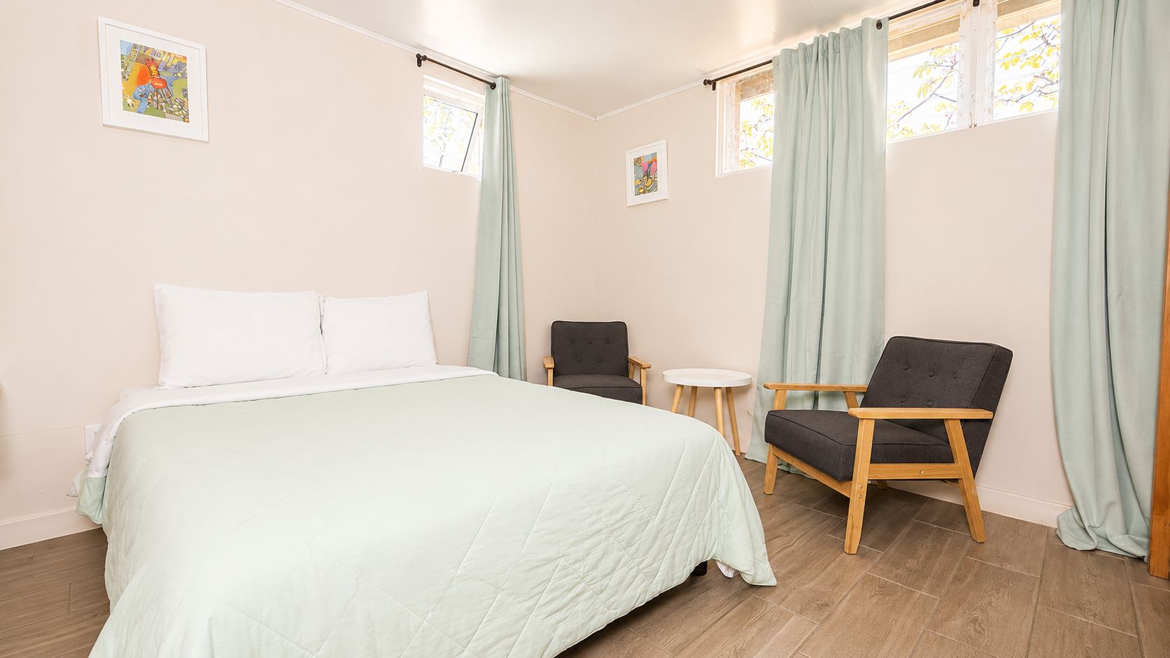 Ett hotellrum med en säng, två stolar, ett litet bord och två fönster med gardiner.