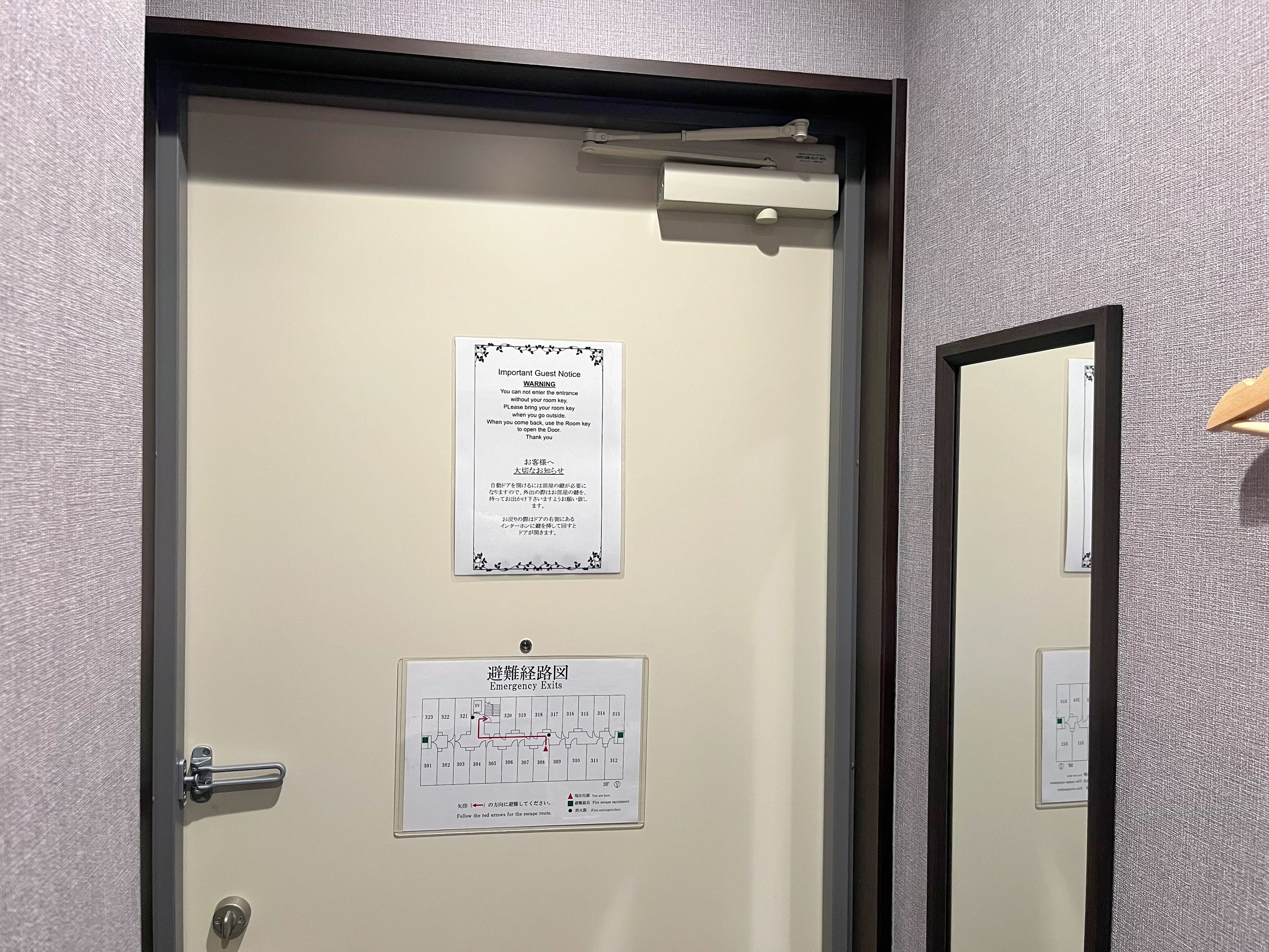 A hotel room door with a notice about room key usage and an emergency exit map.