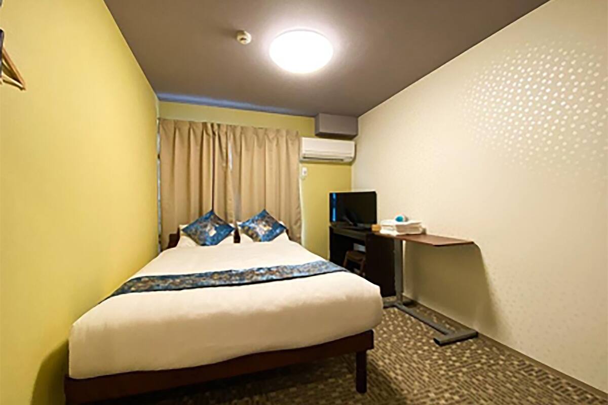 A hotel room with a bed, a desk, a television, and an air conditioning unit.