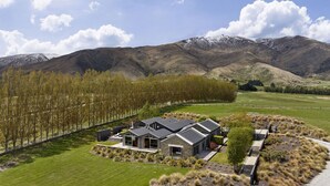 A modern house with a large lawn, a driveway, and a view of mountains. - Kumanu - Crown Range (Arrow Junction)