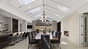 A modern dining area with a long table and chairs, a chandelier, and a fireplace. - Kumanu - Crown Range (Arrow Junction)
