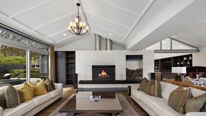 A spacious living room with a fireplace, large windows, and a modern chandelier. - Kumanu - Crown Range (Arrow Junction)