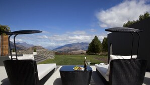 A patio with two black wicker sofas, a round table with a bottle and glasses, and a view of mountains. - Kumanu - Crown Range (Arrow Junction)