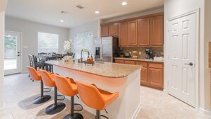 Une cuisine moderne dotée d’un îlot central, de meubles en bois et d’un coin salon avec des chaises orange.
