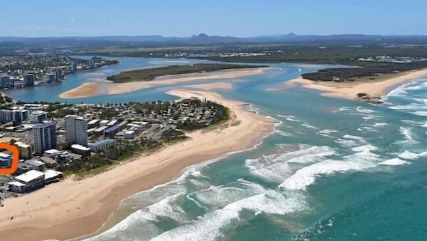 Vue aérienne d’une zone côtière comprenant une plage, un port de plaisance et un quartier résidentiel avec des immeubles de grande hauteur.
