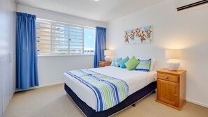 Une chambre à coucher comprenant un lit, deux tables de chevet, une fenêtre avec des rideaux, un climatiseur fixé au mur et un tableau.