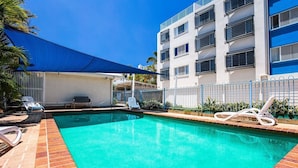 Une piscine avec des chaises longues, un espace de détente couvert et un bâtiment doté de balcons.